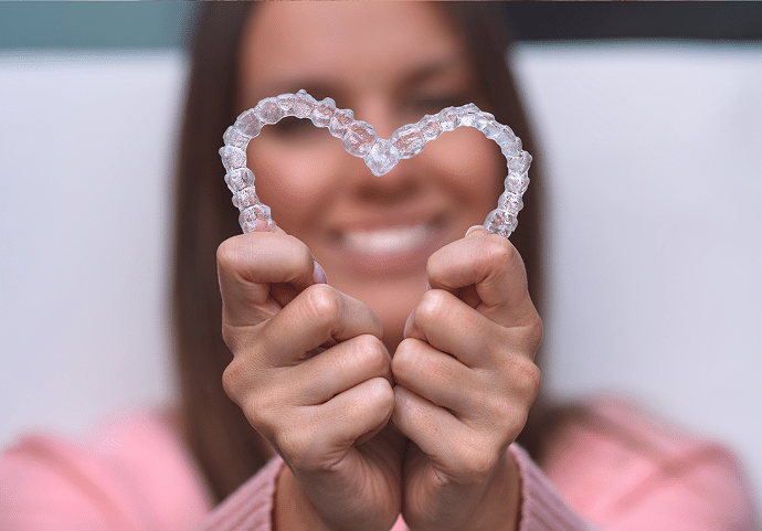Woman with clear aligners smiling holding her aligners in the shape of a heart