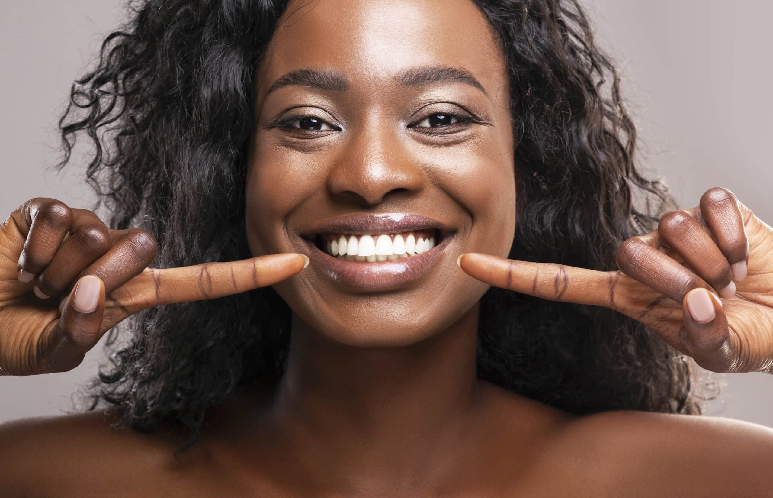 Close up of a photogenic woman pointing at her smile with both hands