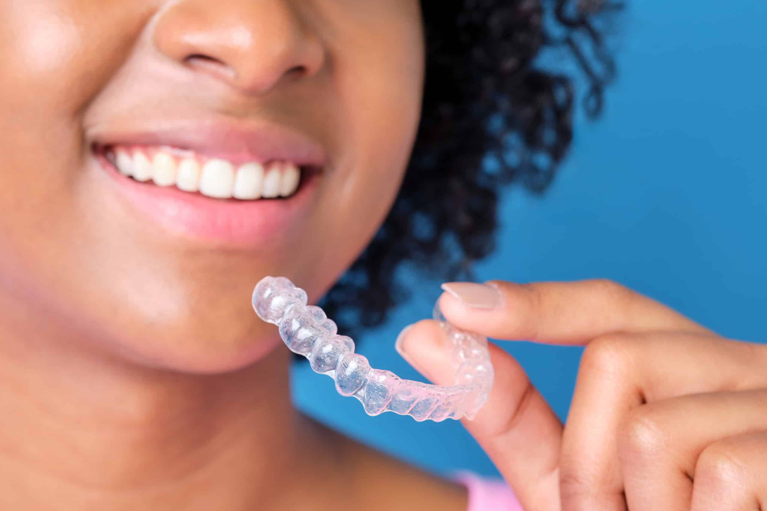 Woman with curly hair smiles as she inserts clear aligners