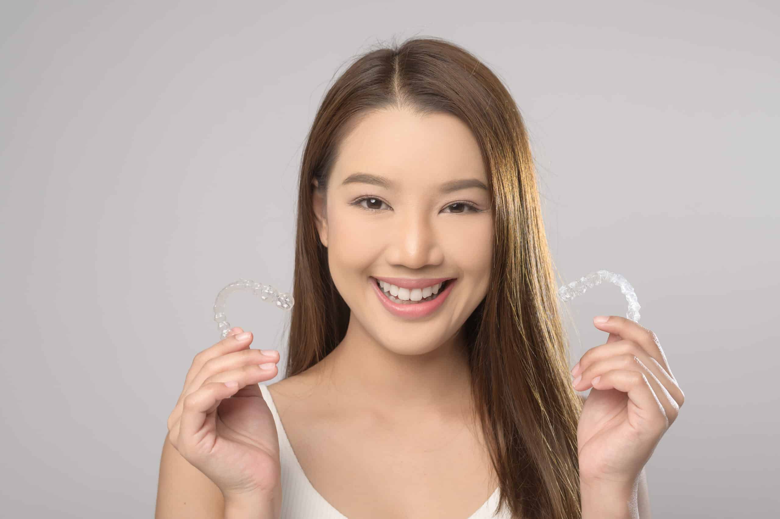 Smiling woman holding invisalign braces over white background